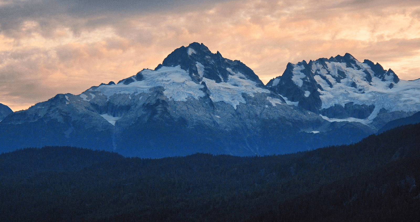 Landscape shot of 2 snowy mountains with a forest below them